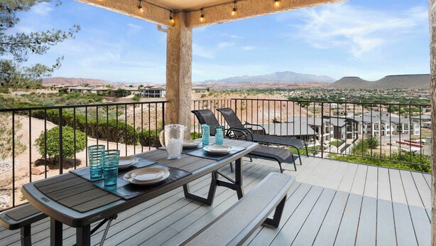 Un espacio comedor al aire libre cubierto con una mesa preparada para dos, con vistas a una zona residencial y montañas al fondo.