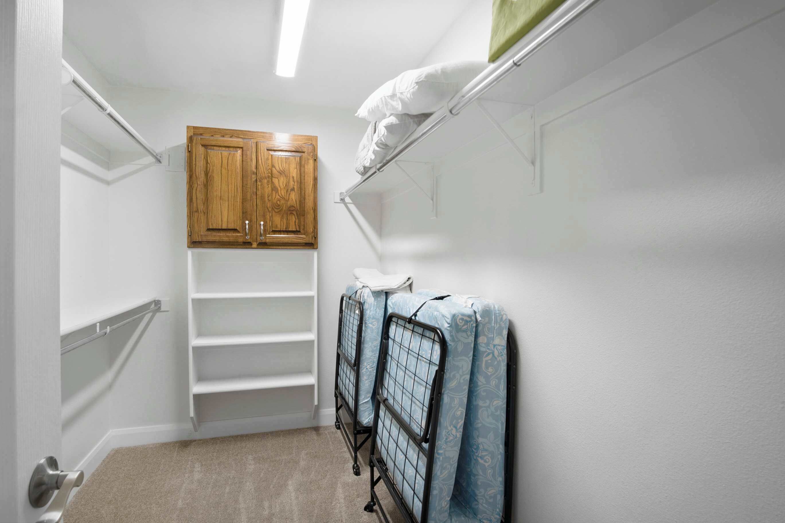 A narrow hallway with a wooden cabinet, a metal rack with folded mattresses, and a white door.