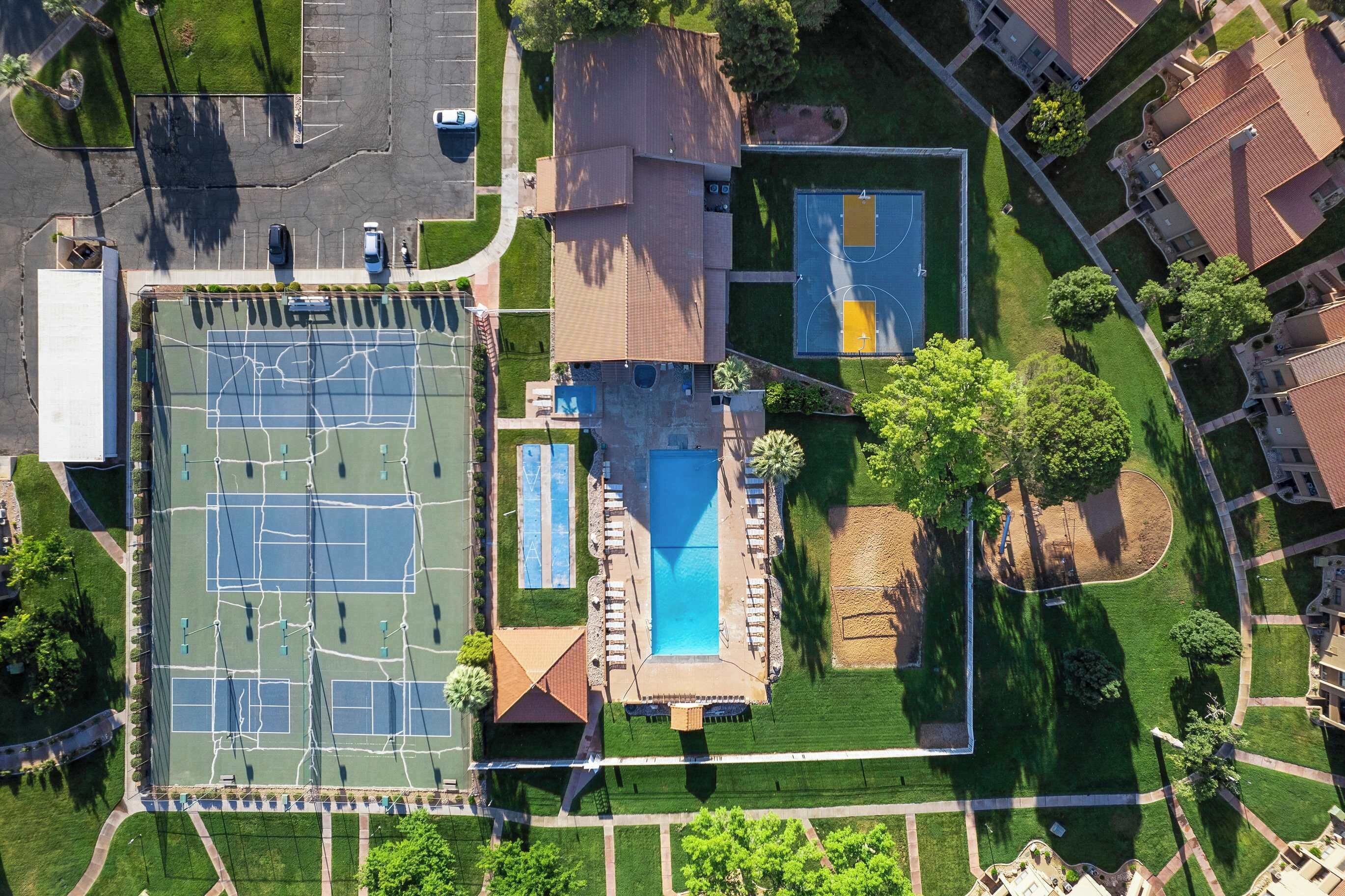 Vista aérea de um complexo esportivo com várias quadras de tênis, uma piscina e uma quadra de basquete.
