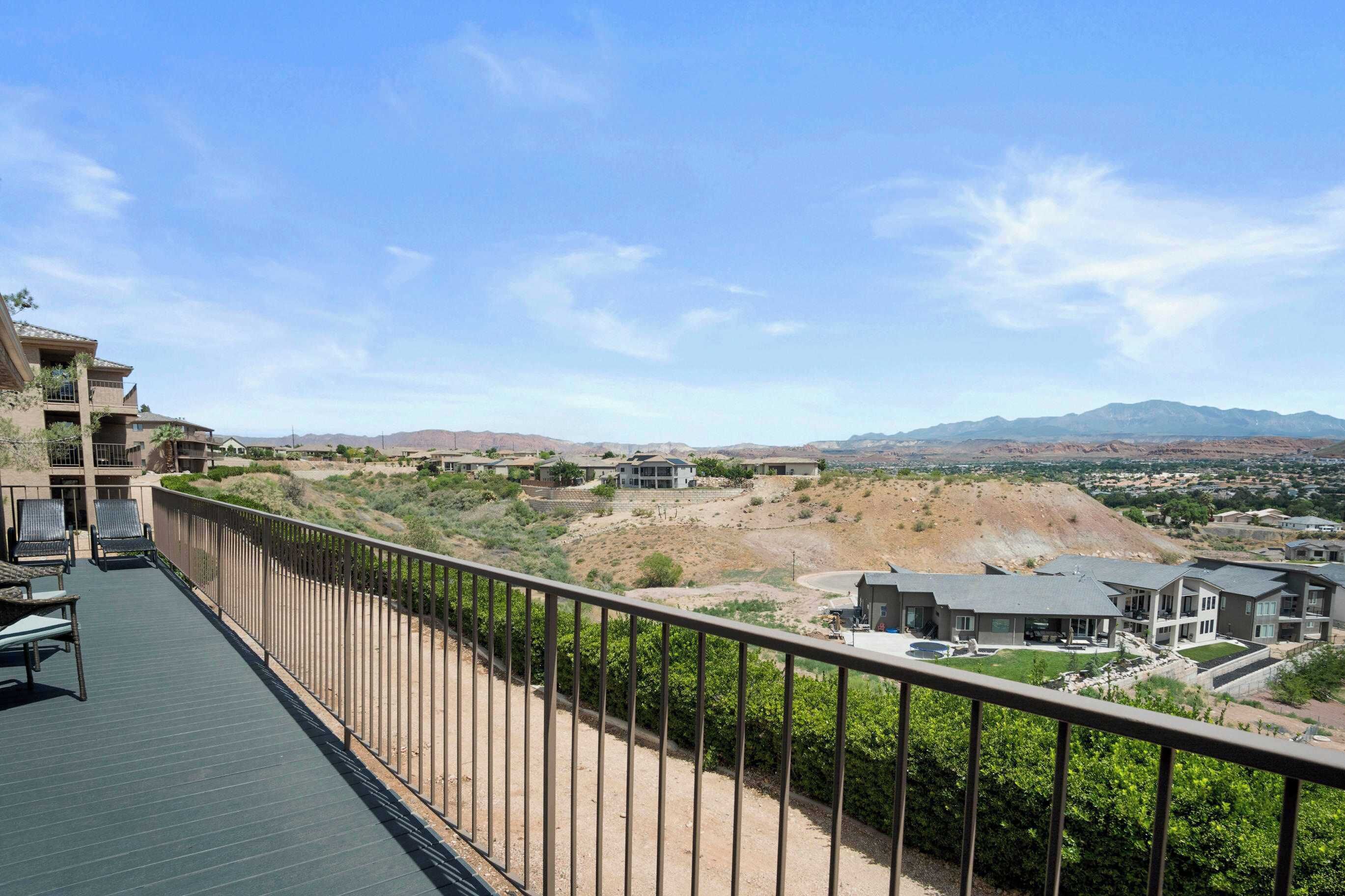 A balcony with a view of a residential area, including houses and a hilly landscape.