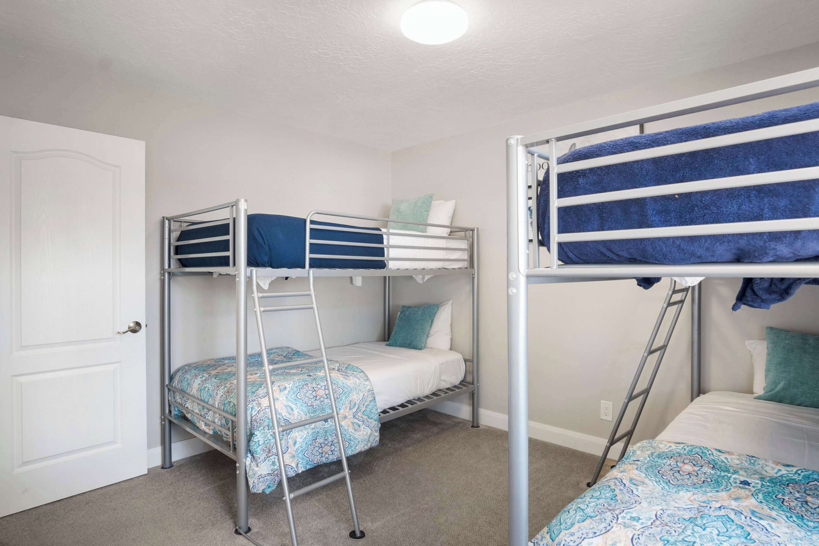 Une pièce avec deux lits superposés, une porte et un luminaire au plafond.