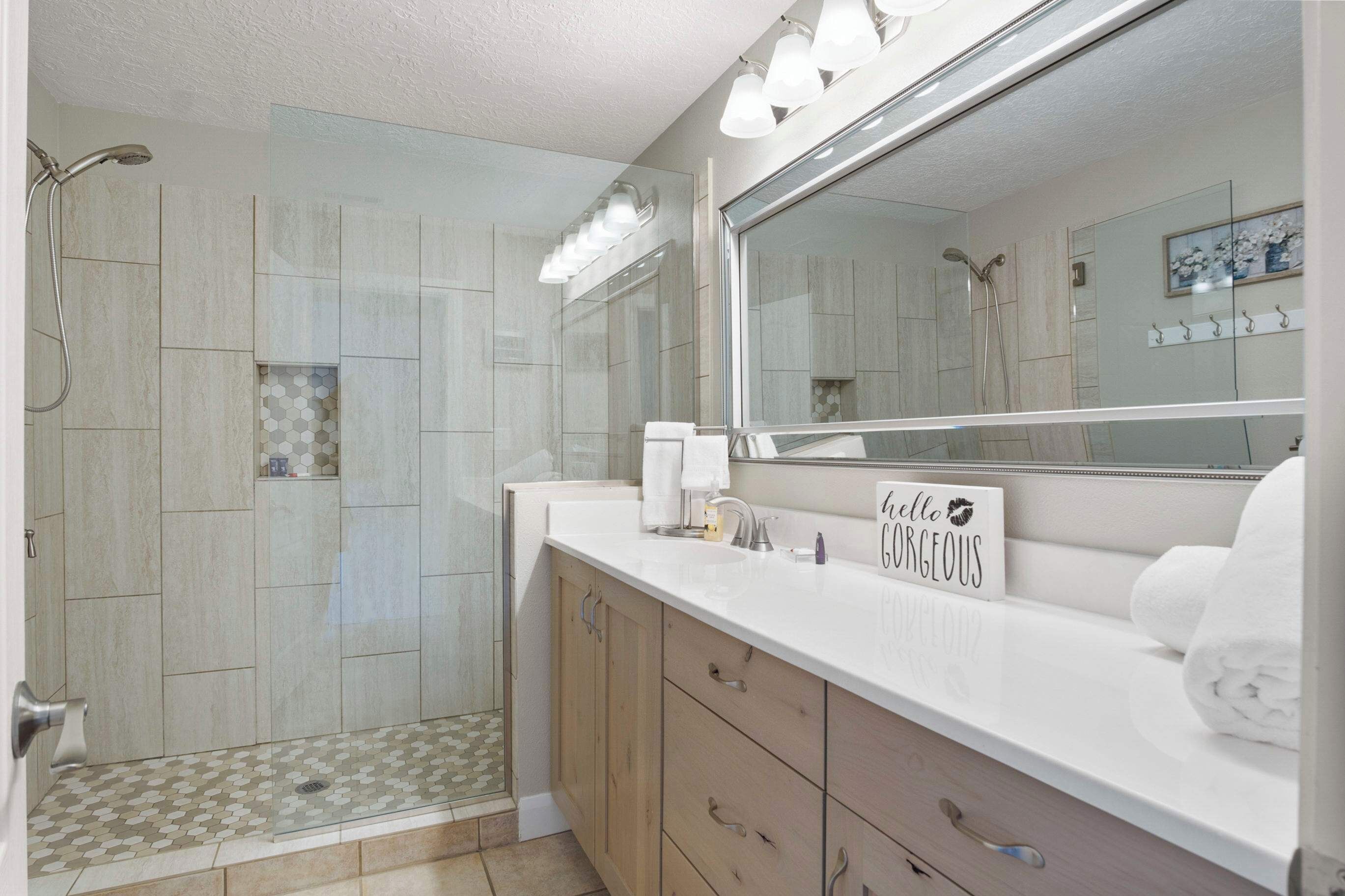Un baño moderno con ducha de vidrio, un espejo grande y tocador con perchero.
