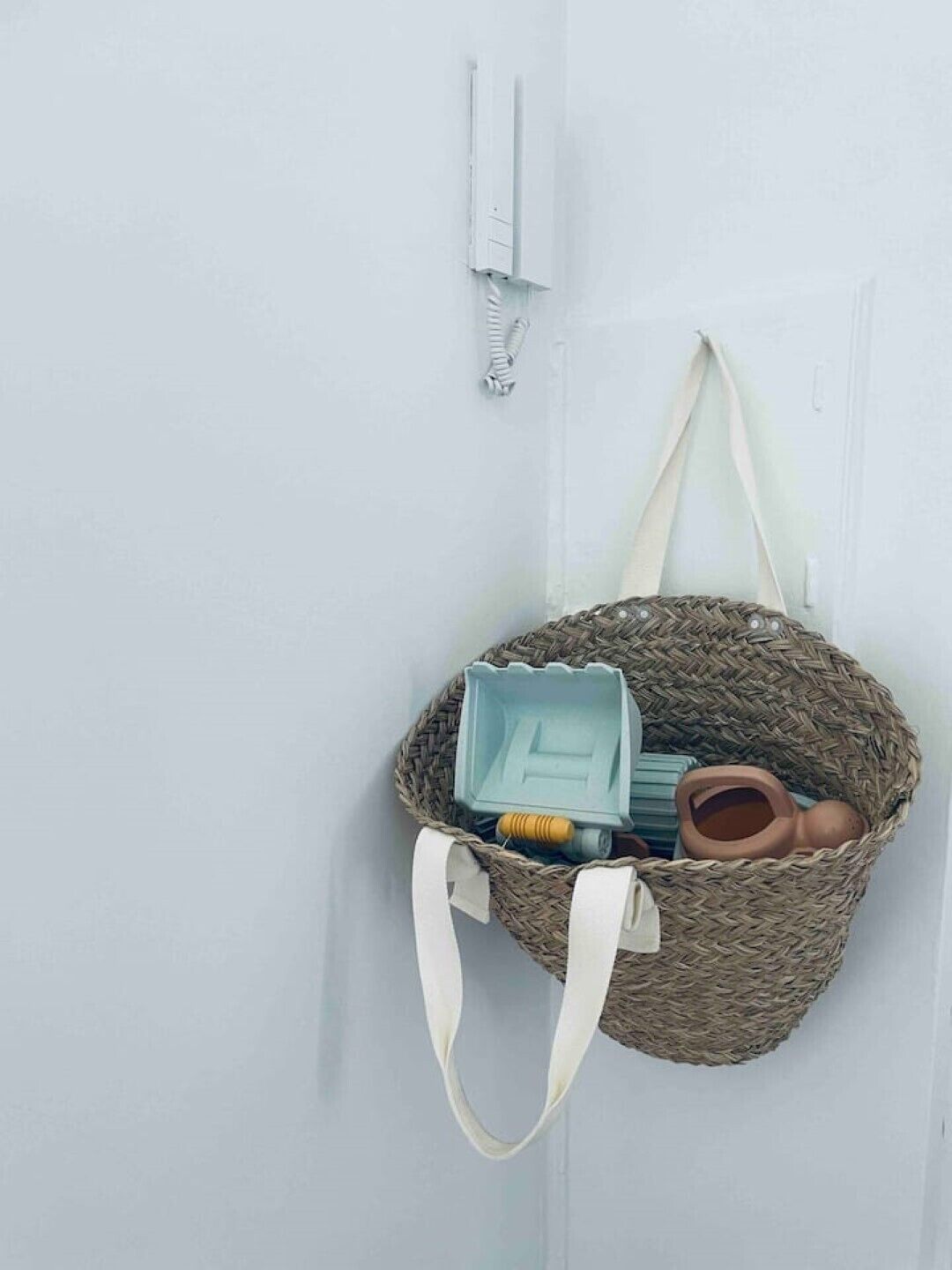 A woven bag with handles hanging on a white door.