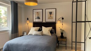 Ett sovrum med en säng, sängbord, en hängande lampa och inramade konstverk på väggen.