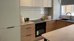 Ett modernt kök med vita skåp, en svart ugn, en diskho och ett fönster med utsikt över en byggnad med tegelstensfasad.
