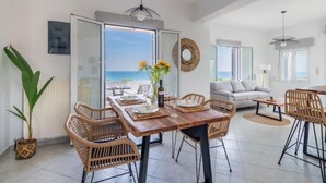 A spacious living area with a wooden dining table, wicker chairs, and a view of the sea through large glass doors. - Blue Harmony villa SEA VIEW heated pool  (ΑΠΟΚΟΡΩΝΑΣ ΧΑΝΙΩΝ)