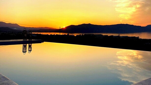 A serene sunset over a calm body of water with a clear reflection, surrounded by mountains and a distant shoreline. - Blue Harmony villa SEA VIEW heated pool  (ΑΠΟΚΟΡΩΝΑΣ ΧΑΝΙΩΝ)