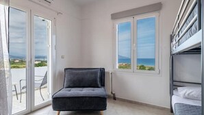 A room with a grey sofa, a bed with white bedding, and a view of the sea through a window. - Blue Harmony villa SEA VIEW heated pool  (ΑΠΟΚΟΡΩΝΑΣ ΧΑΝΙΩΝ)