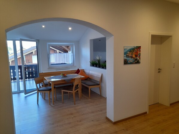 A dining area with a wooden table and chairs, a bench with cushions, a window with a view, and a door leading to another room.
