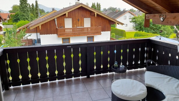 Een balkon met uitzicht op een houten huis, een betegelde vloer en tuinmeubilair.