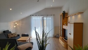 Een moderne woonkamer met een bank, salontafel en planten. Er is een schuifpui naar een balkon.