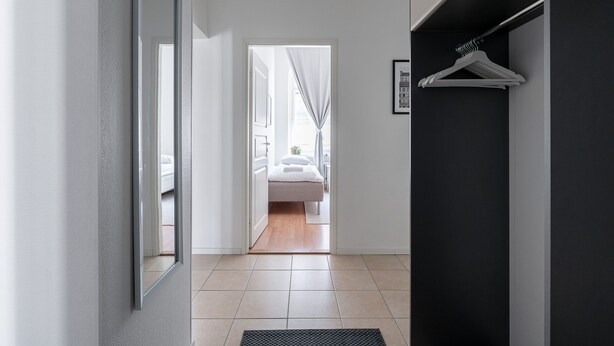 A hallway leading to a bedroom with a bed, a wardrobe, and a hanging clothes rack. - Historical 3BR Downtown Apartment with Sauna (Tampere)