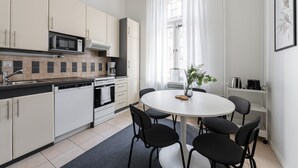 A modern kitchen with white cabinets, a microwave, a stove, and a sink. There is a round table with chairs and a vase with flowers. - Historical 3BR Downtown Apartment with Sauna (Tampere)