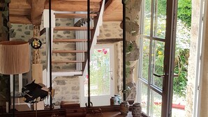 Un interior rústico con una escalera de madera, una mesa con diversos objetos y una ventana con vista a la vegetación.