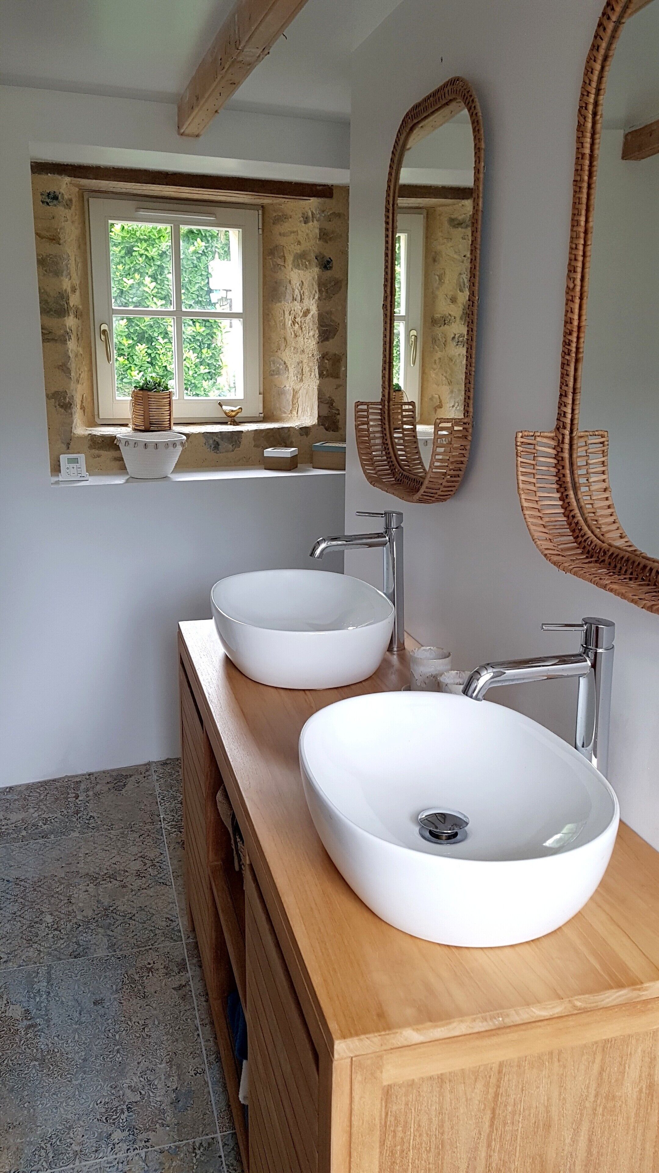 A bathroom with two white sinks, a wooden vanity, a window with a view of greenery, and a large mirror.