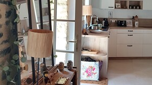 Un interior rústico con pared de piedra, vigas de madera en el techo, una cocina con armarios blancos y un comedor con mesa y sillas.