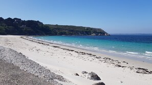 A beach with clear blue water, white sand, and rocky terrain.