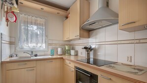 Een moderne keuken met houten kastjes, een roestvrijstalen spoelbak, een ingebouwde oven en een raam met dunne gordijnen.