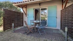 Een terras met een tafel en stoelen, een houten schutting en een gebouw met blauwe luiken.