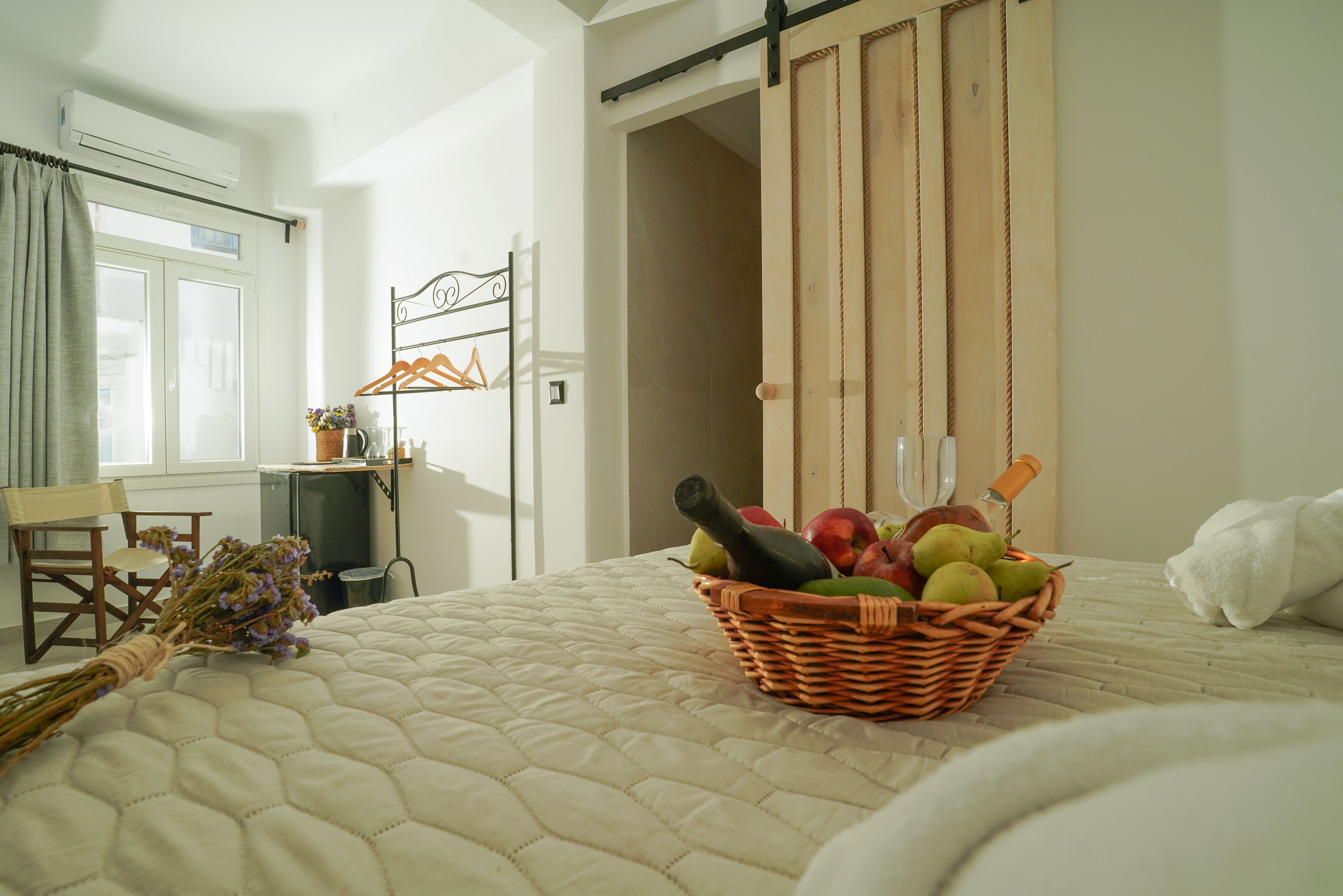 A bedroom with a bed, a wicker basket of fruits and a bottle, a desk with a chair, and a sliding door.