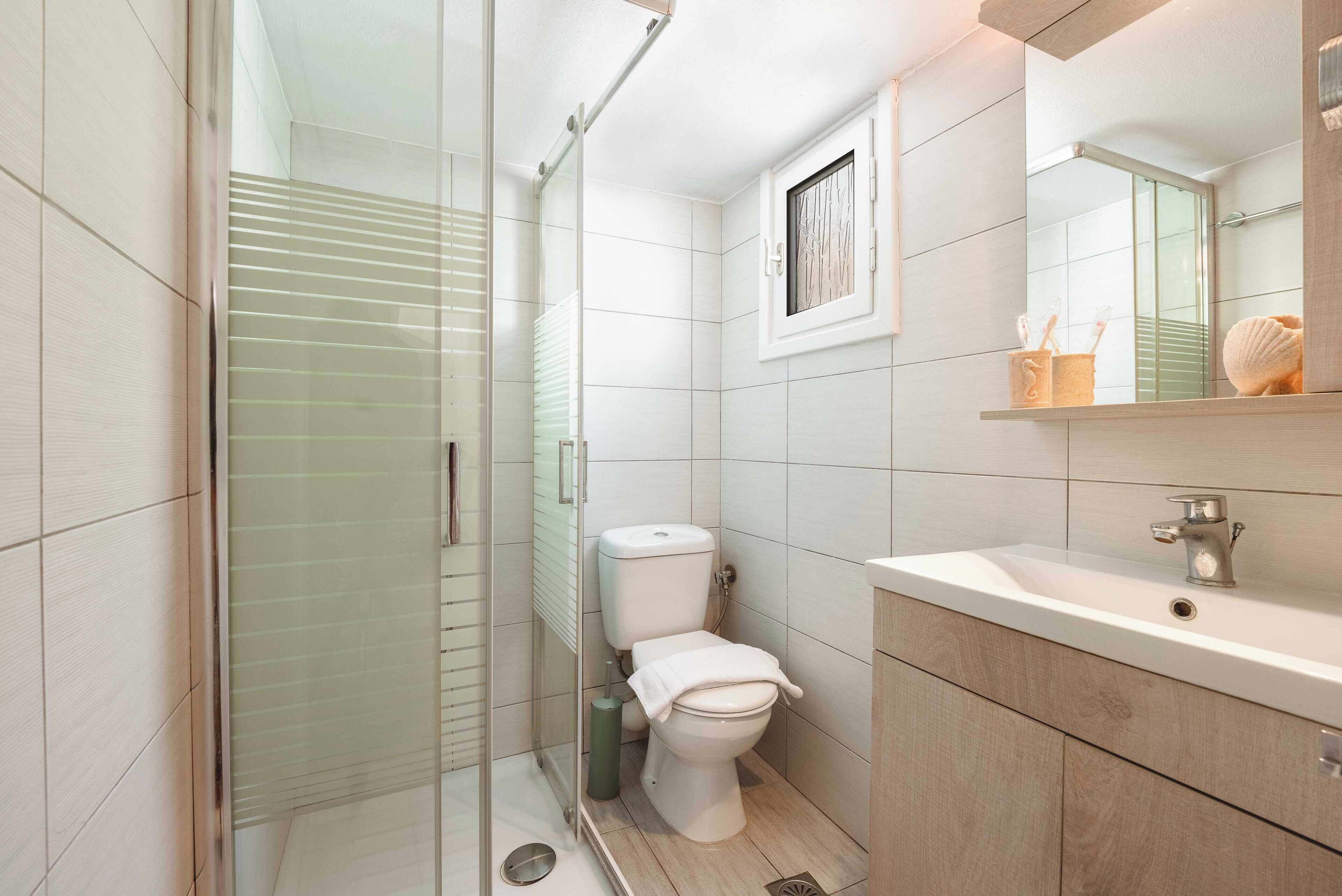 Un bany modern amb una dutxa amb mampara de vidre, un vàter, un lavabo amb mirall i un escurapulides.