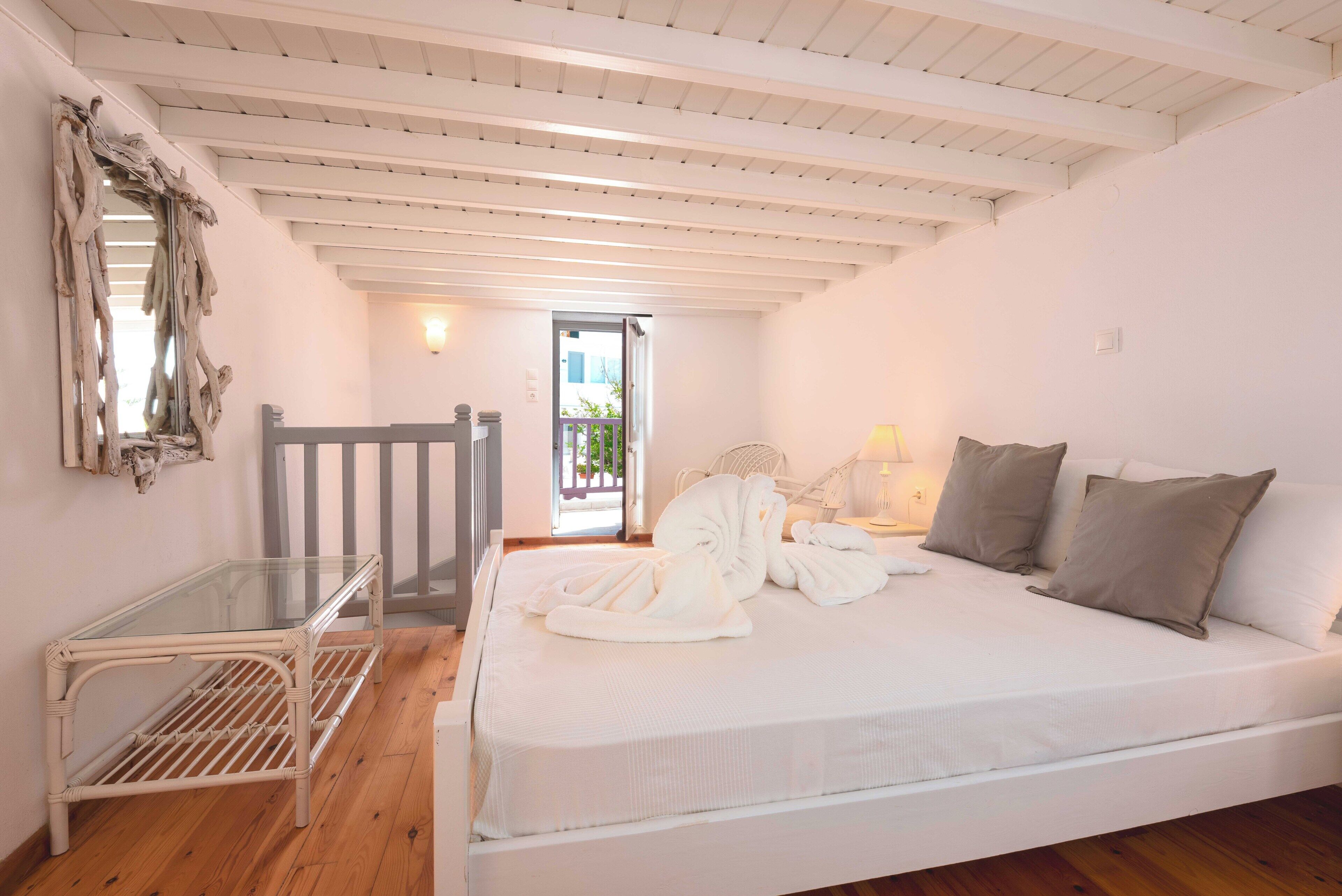 A bedroom with a bed, a glass-top table, a chair, a mirror, and a door leading outside.