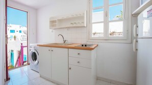 Une cuisine compacte équipée d’un lave-linge, d’un évier et d’une fenêtre donnant sur des immeubles.