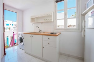 Cozinha compacta com máquina de lavar, pia e janela com vista para edifícios.