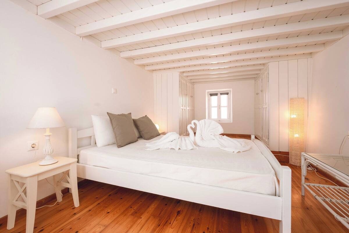 Un lit blanc avec des serviettes, une table de chevet avec une lampe et un plancher en bois.