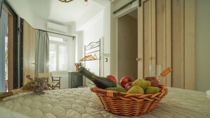 Une chambre à coucher avec un lit, un panier en osier rempli de fruits et une bouteille, une fenêtre et une porte.