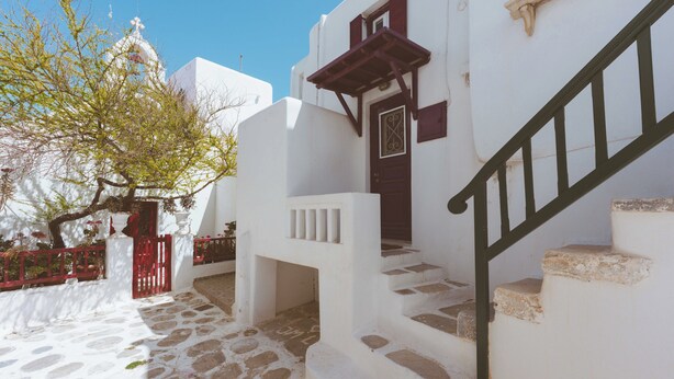 Un bâtiment blanc avec une porte rouge, des marches en pierre et un escalier doté d’une rampe verte.