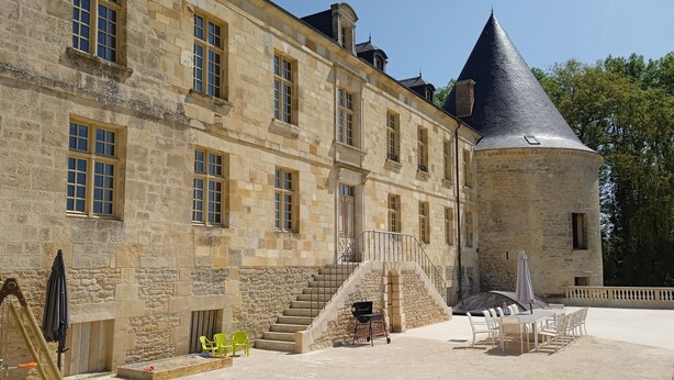 A historic stone building with a conical tower, a staircase leading to a covered area with outdoor seating. - Château à 5mn des Sentiers (Charbogne)