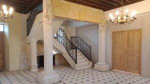 A spacious interior with a grand staircase, white columns, and a patterned floor. - Château à 5mn des Sentiers (Charbogne)