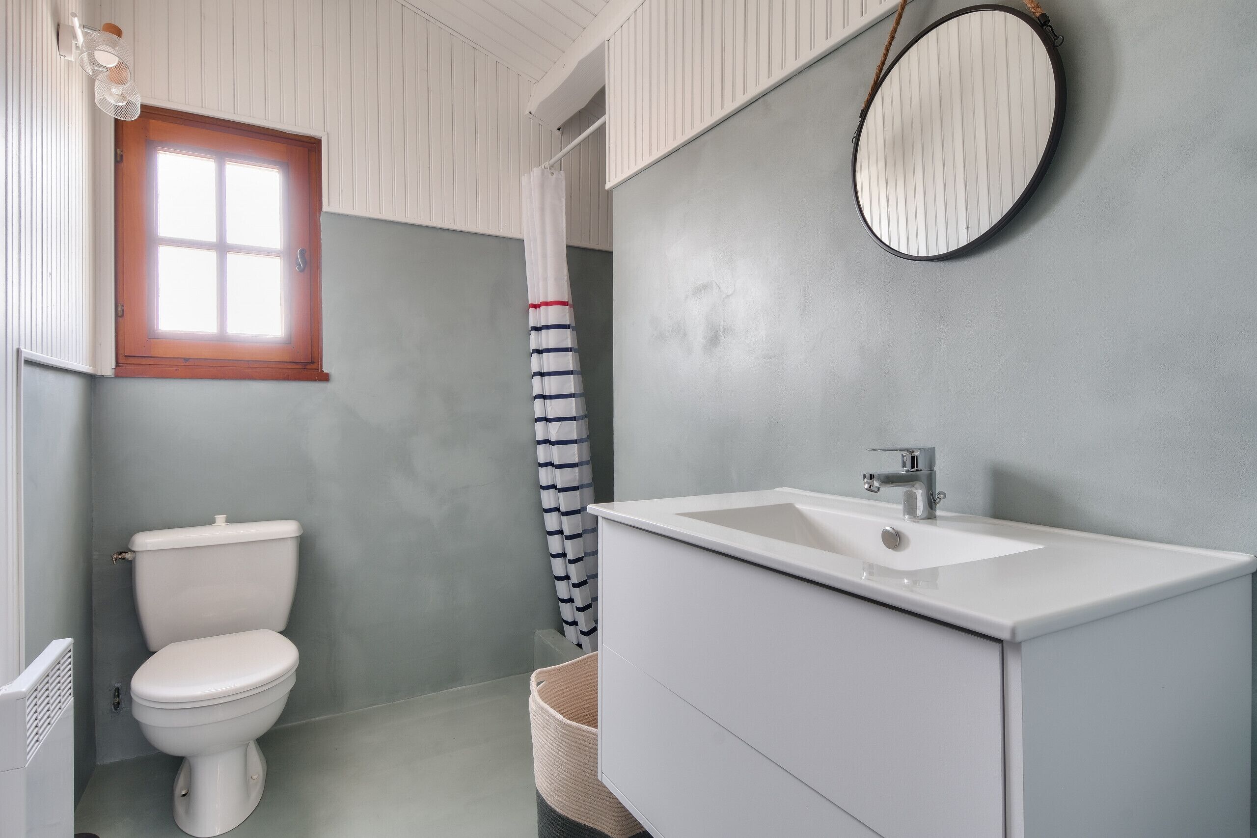 A bathroom with a white toilet, a white sink, and a window with a wooden frame.