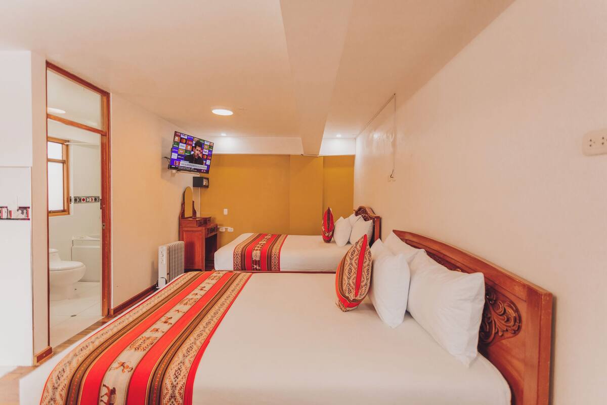 A hotel room with two beds, a television mounted on the wall, and a bathroom visible through an open door.