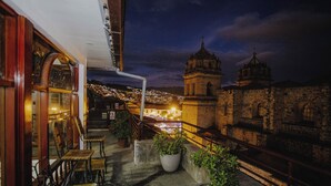 A balcony with potted plants, wooden chairs, and a railing overlooking a historic building with domed towers. - Quechua Hotel cusco (Cusco)