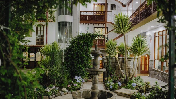 A courtyard with a stone fountain, lush greenery, and a traditional building with wooden balconies. - Quechua Hotel cusco (Cusco)