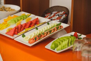 Una mesa de buffet con diversas frutas y verduras cortadas dispuestas en platos blancos.