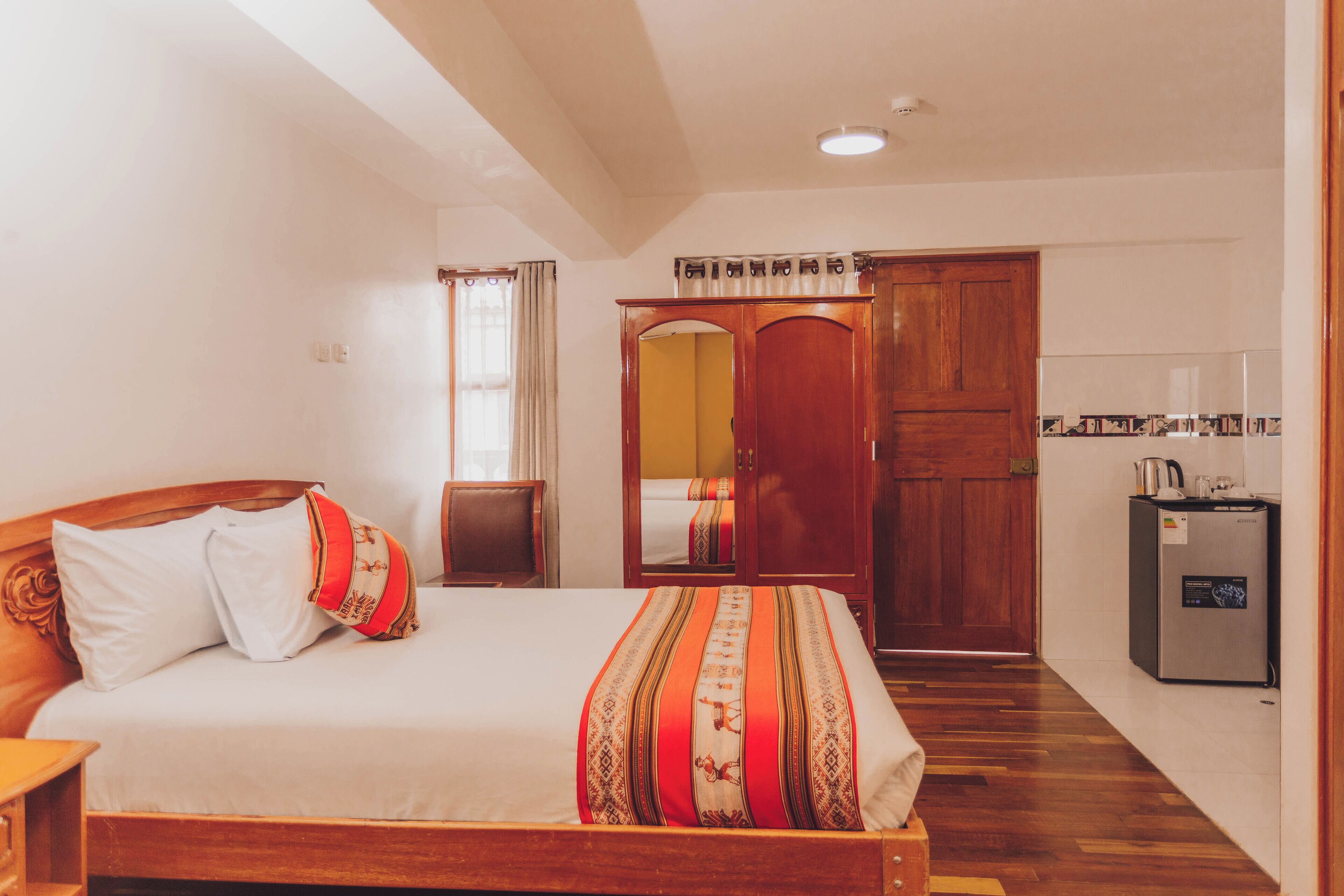 A hotel room with a wooden bed, a wardrobe, a small kitchenette, and a mirror.