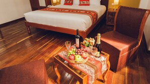 A hotel room with a wooden bed, a nightstand, a table with fruits and drinks, and a chair. - Quechua Hotel cusco (Cusco)