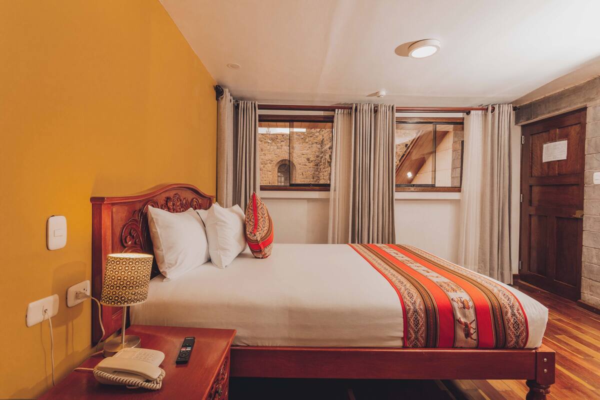 A hotel room with a wooden bed, a bedside lamp, a telephone, and a window with curtains.