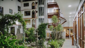 A multi-story building with a central courtyard featuring a fountain, surrounded by lush greenery and stone walls. - Quechua Hotel cusco (Cusco)