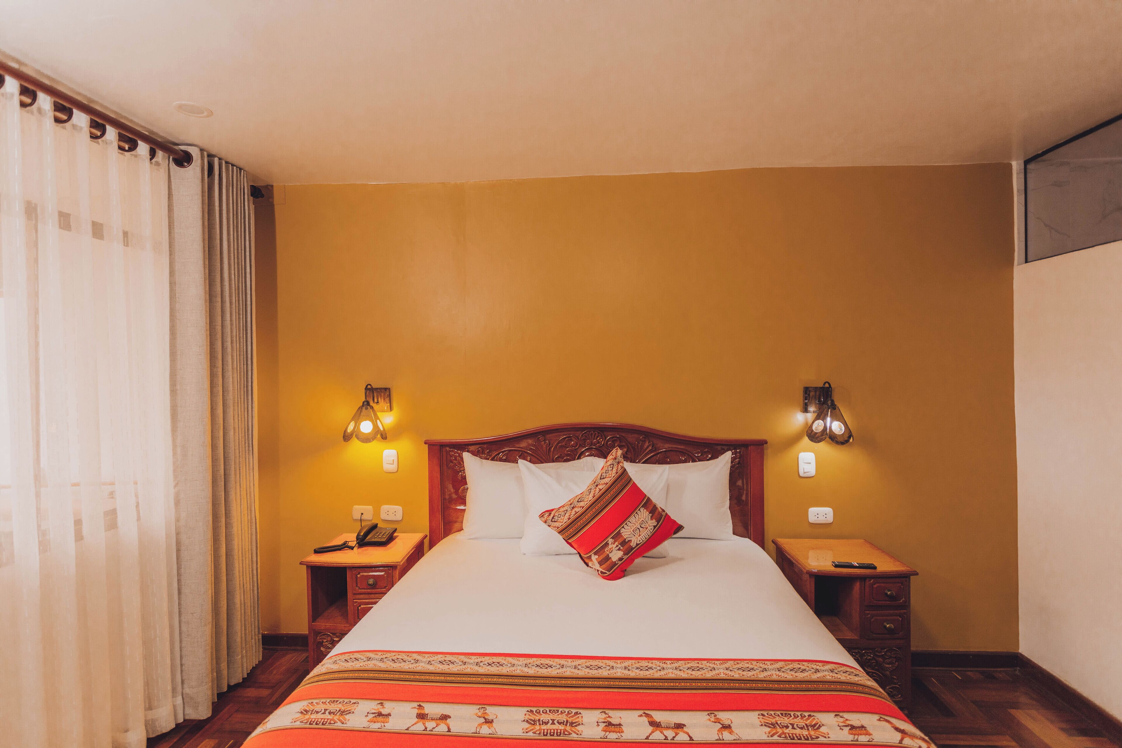 A hotel room with a large bed, two bedside tables, and a curtain on the window.