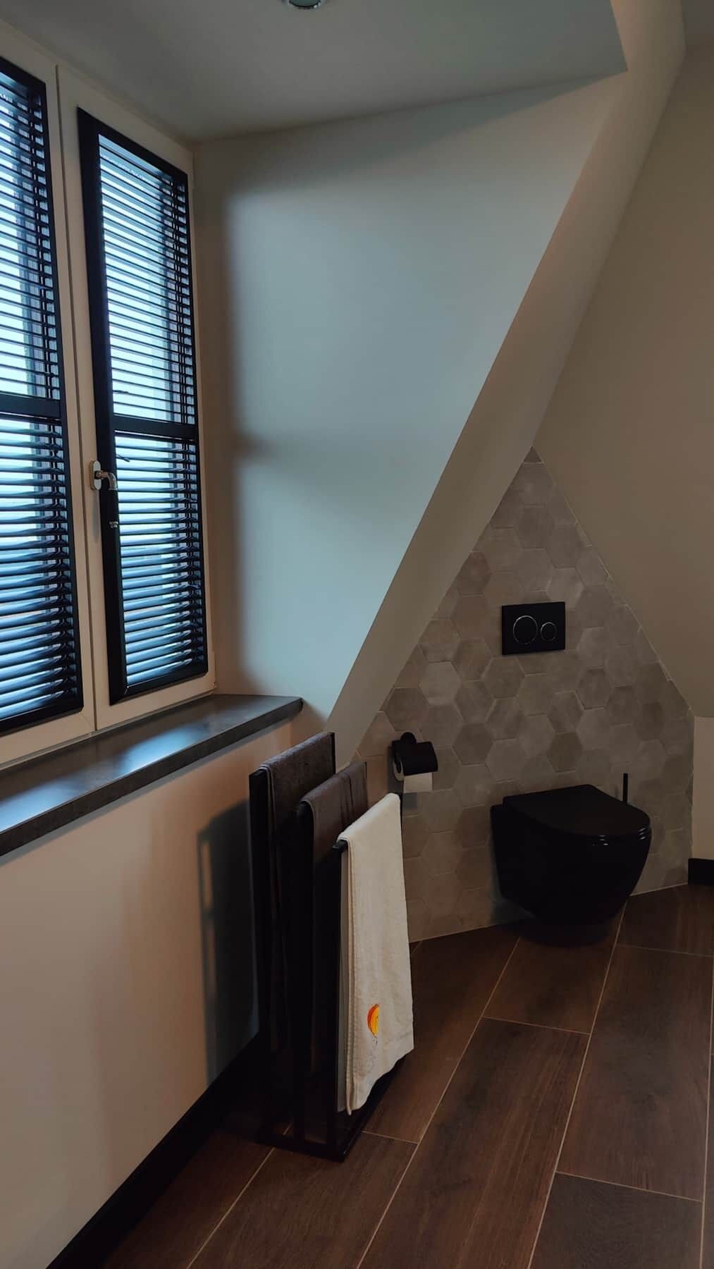 A corner of a room with a window, a radiator, a towel on a chair, and a black toilet.