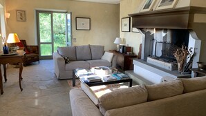 A living room with a sofa, coffee table, fireplace, and a door leading to a garden. - Podere Fontebernardi, authentic Tuscan farmhouse overlooking Pienza. (Monticchielli)