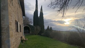 A stone building with a grassy yard, a bench, and tall trees. - Podere Fontebernardi, authentic Tuscan farmhouse overlooking Pienza. (Monticchielli)