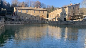 A stone building with a courtyard and a body of water. - Podere Fontebernardi, authentic Tuscan farmhouse overlooking Pienza. (Monticchielli)