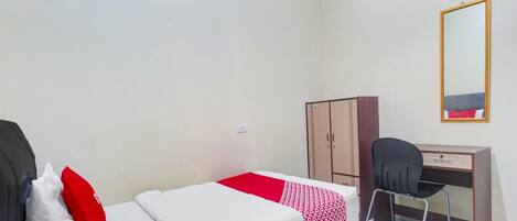 A single bed with a white and red bedspread, a wooden wardrobe, a desk with a chair, and a mirror on the wall.
