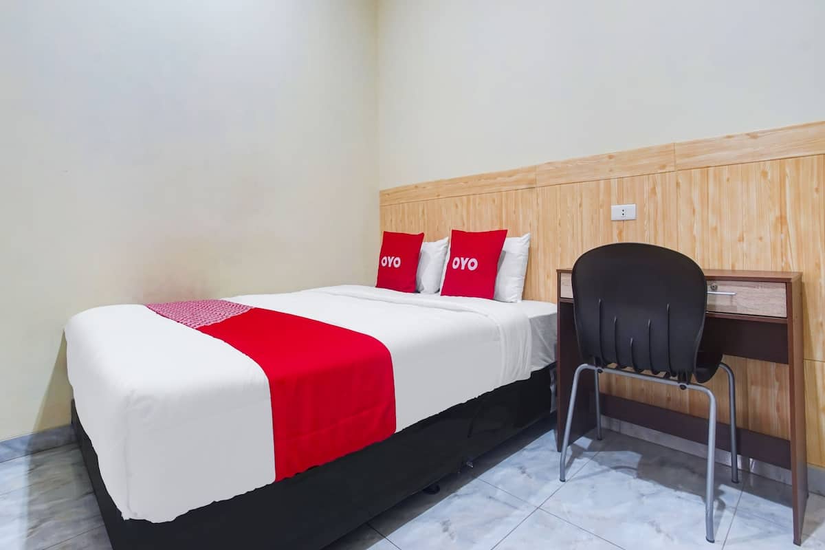 Ein Hotelzimmer mit einem Bett, zwei roten Kissen, einem schwarzen Stuhl und einem hölzernen Kopfteil.