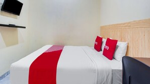 Habitación de hotel con cama, televisor montado en la pared y cabecero de madera.